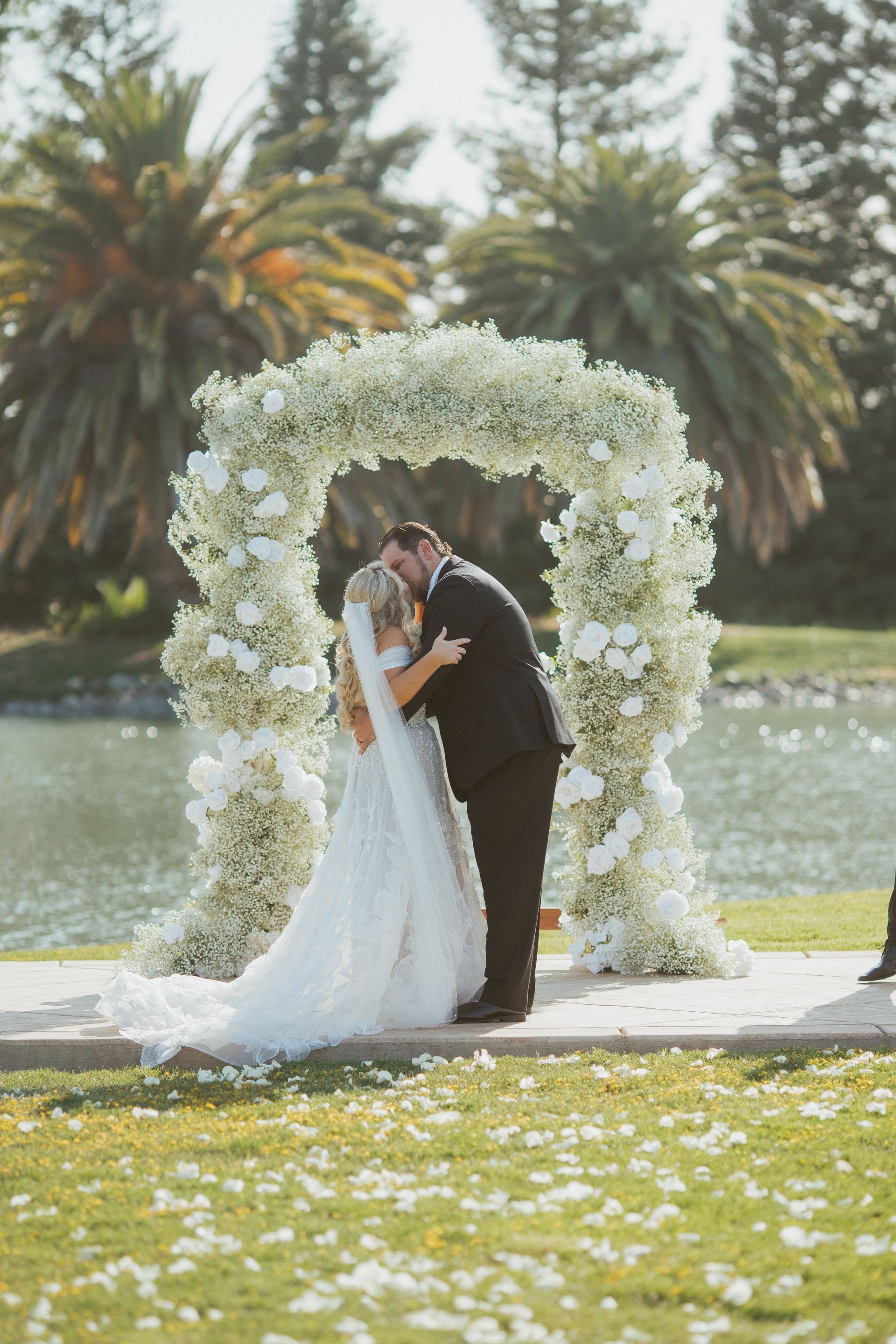 A bride and groom kissing under a floral arch at their wedding ceremony.