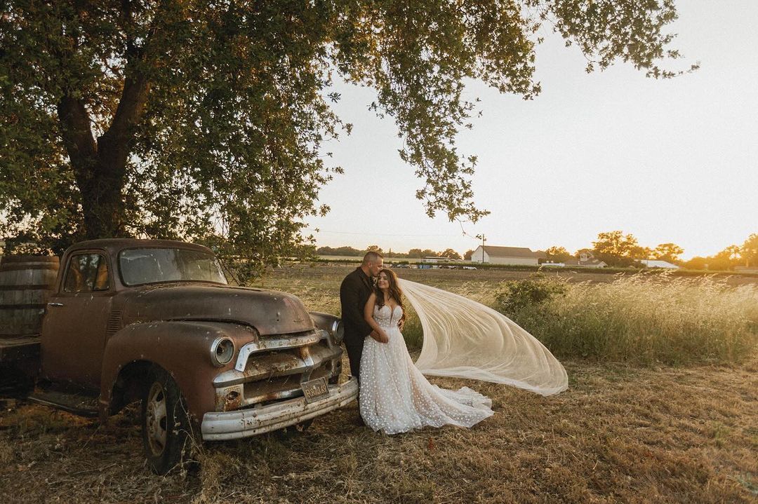 A bride and groom are standing next to an old truck in a field.