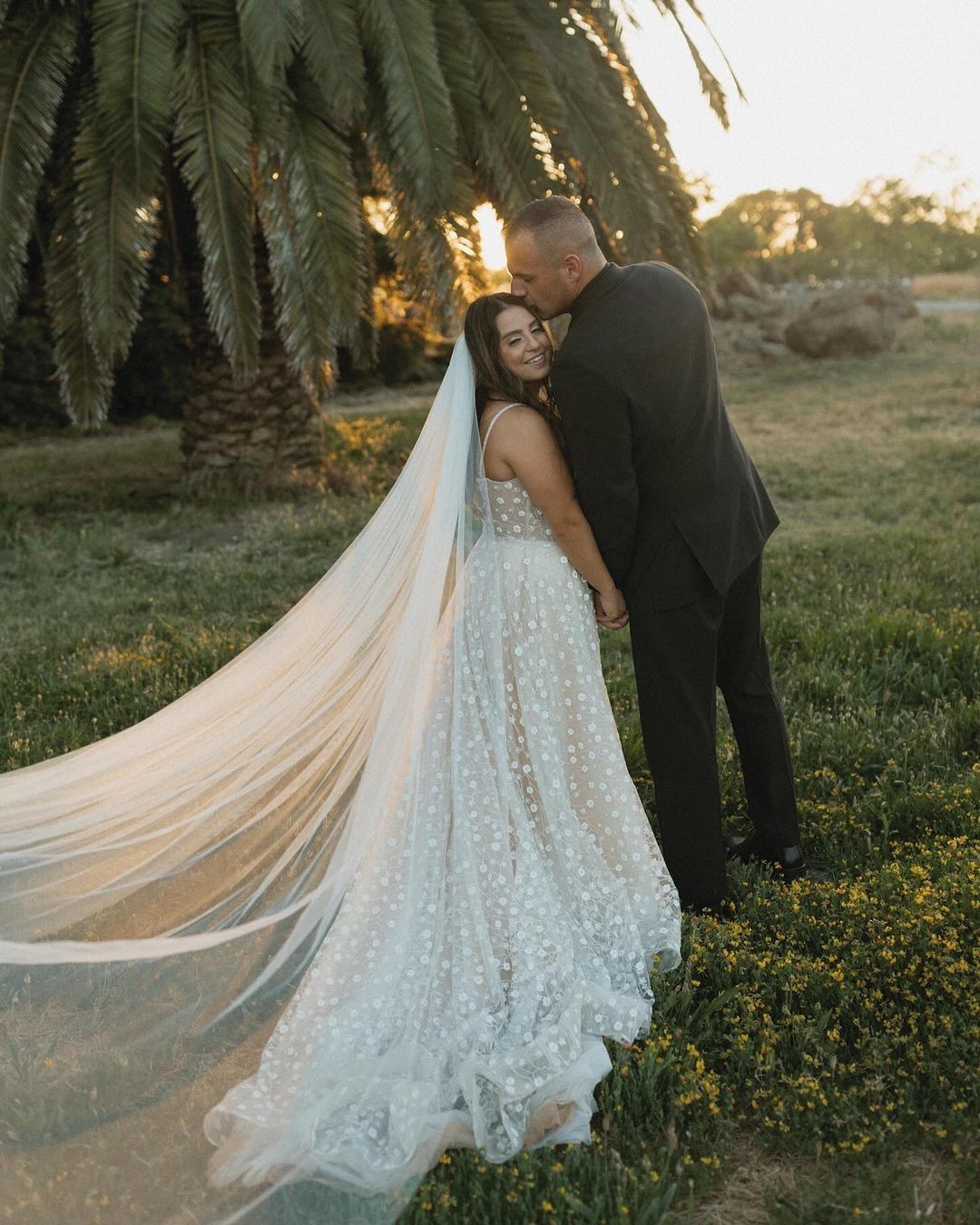 A bride and groom are kissing in a field with a long veil blowing in the wind.