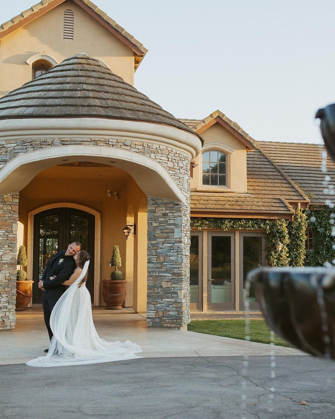 A bride and groom standing in front of a large house