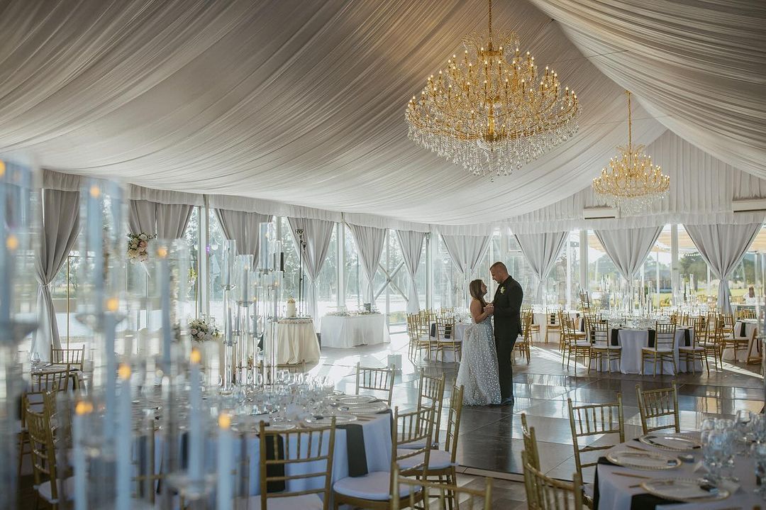 A bride and groom are dancing under a tent at a wedding reception.