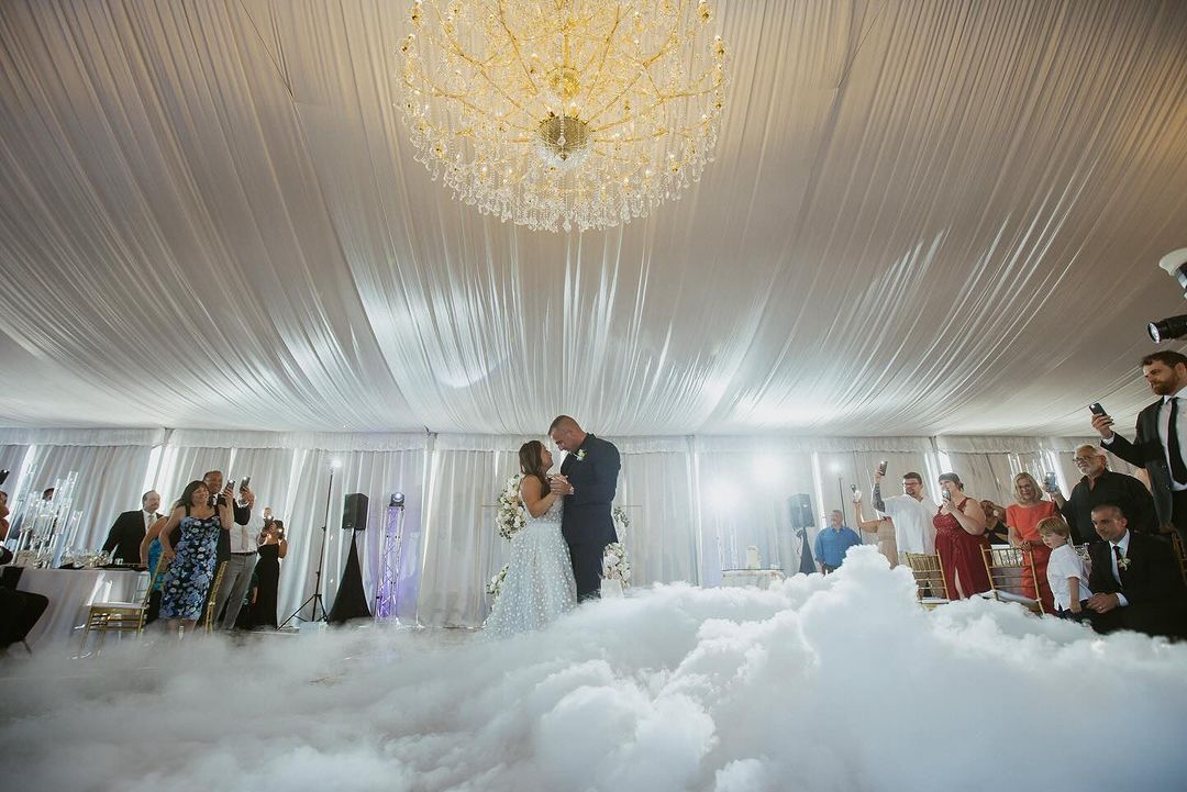 A bride and groom are dancing in a tent with smoke coming out of the ceiling.