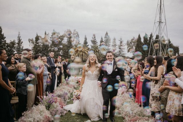 newly married couple walks towards the camera smiling between invited wedding guests