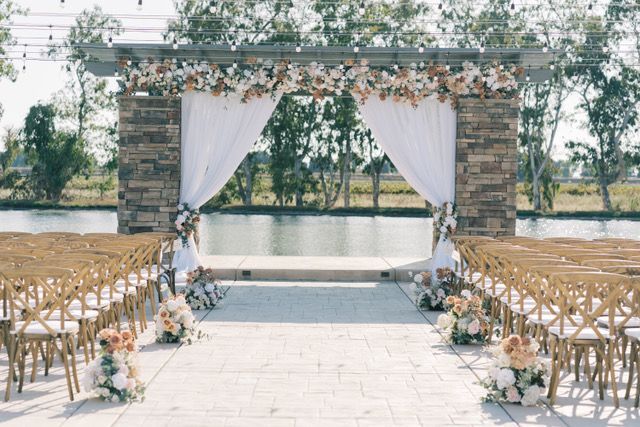 photo of brick alter with flower arrangements bordering the top and bottom of the alter looking out on a lake background with wooden seating in the foreground facing the alter