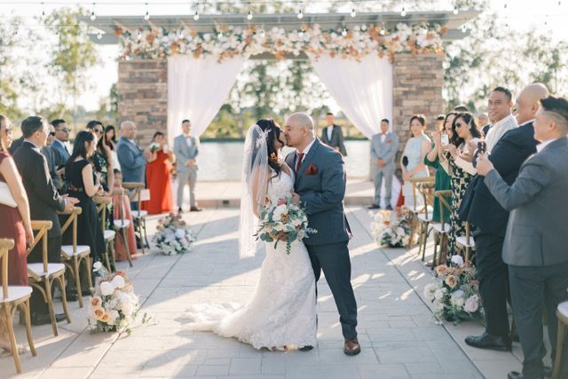 newly married man and woman embrace each other and kiss in focus while the bridal party and groomsmen watch the two kiss in the background