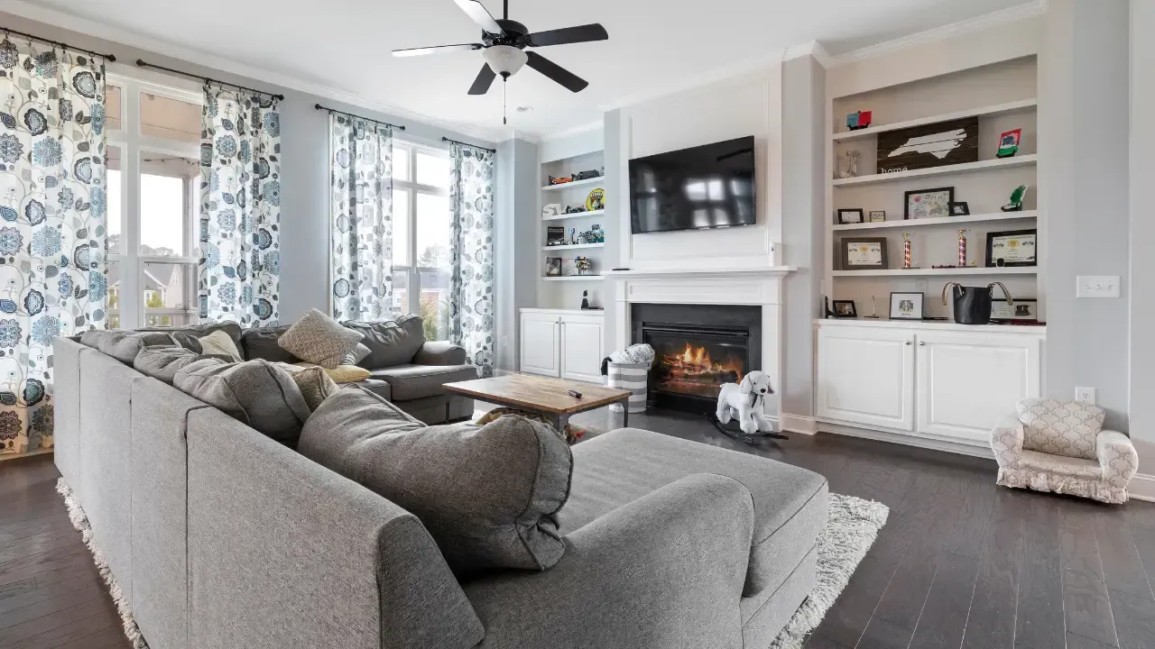 Living room with gray sectional, fireplace, built-in shelves, and patterned curtains.