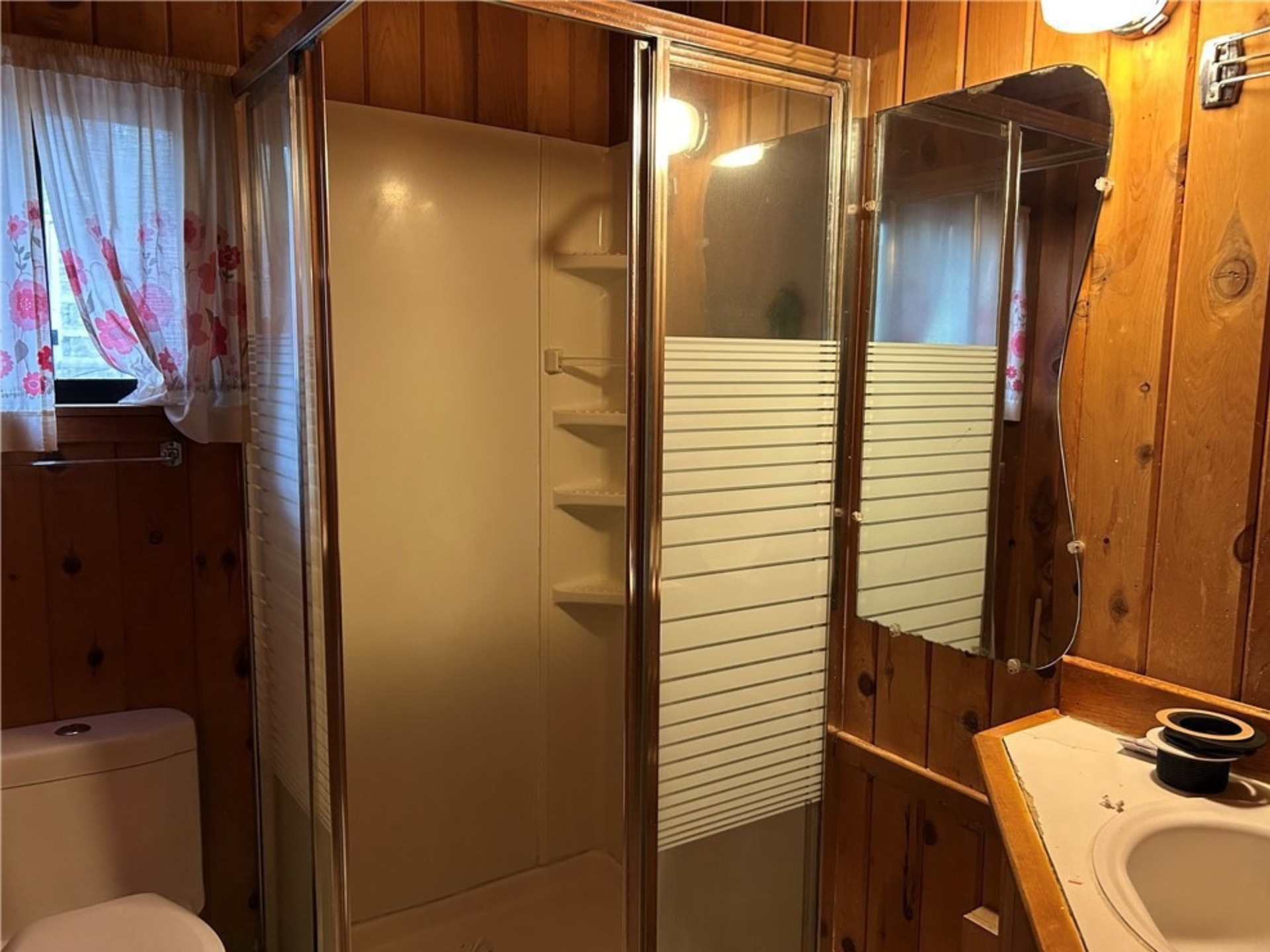 Small bathroom with a shower, toilet, and vanity against wood paneling.