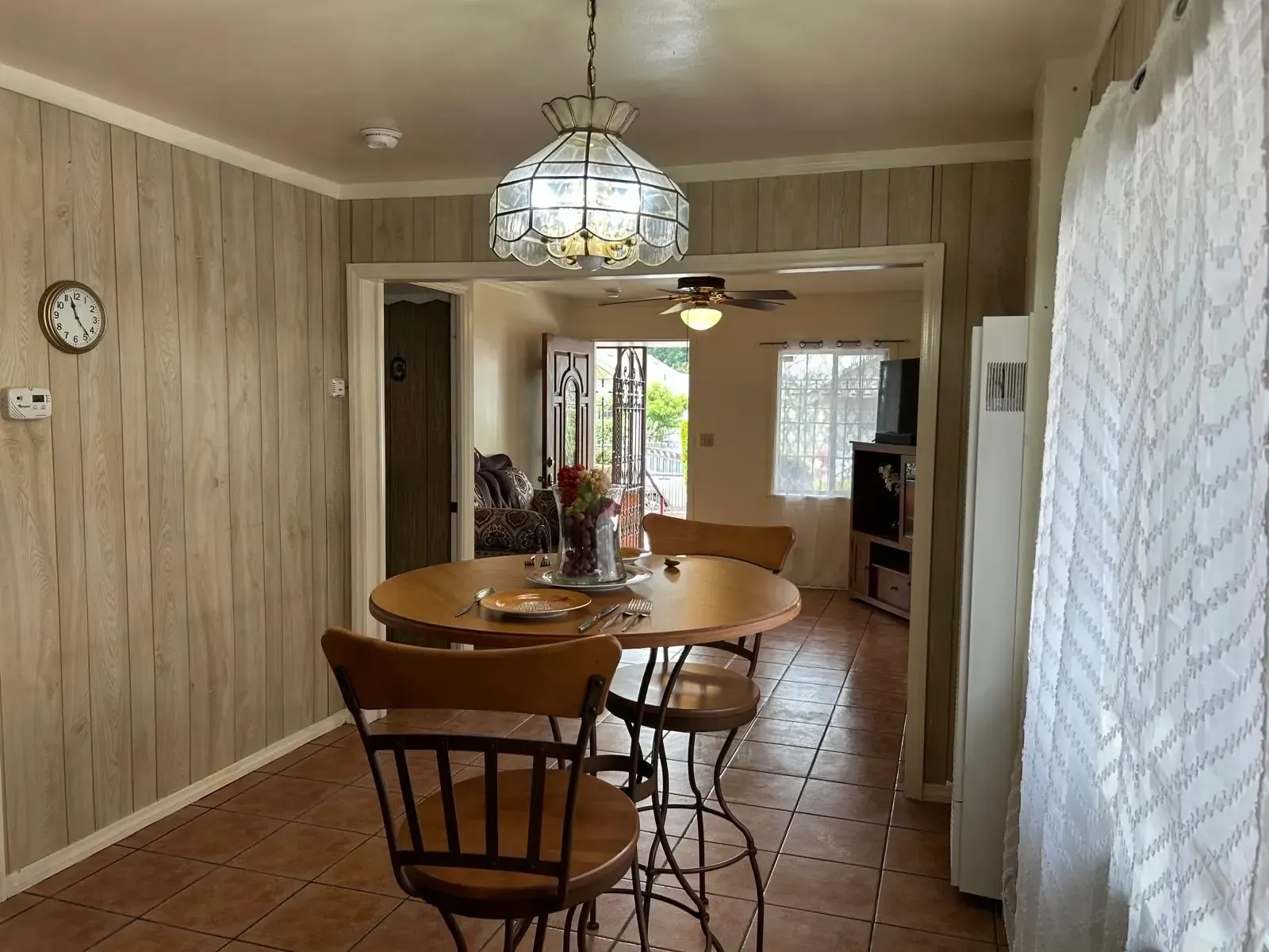 A dining room with a table and chairs and a clock on the wall.