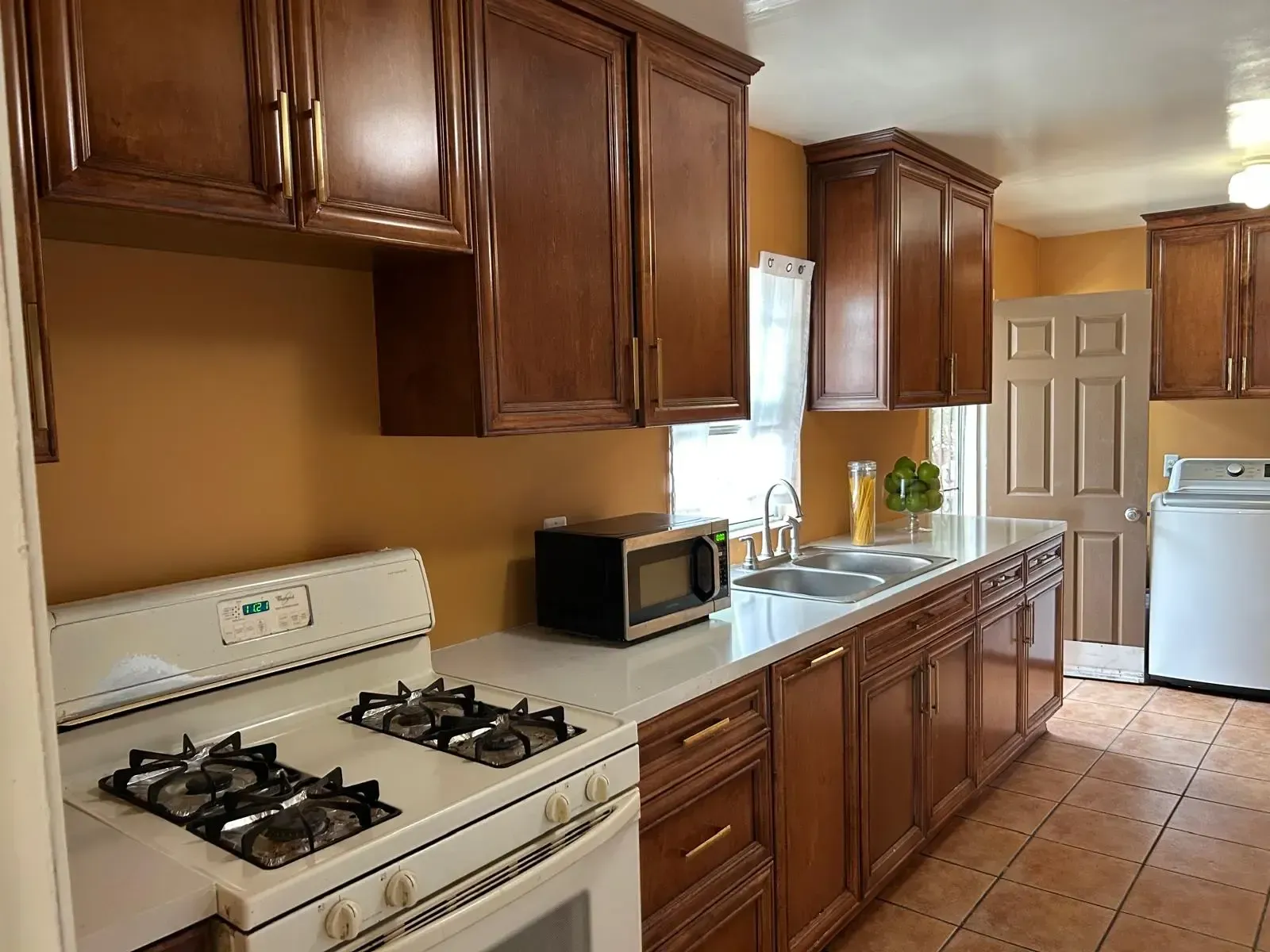 A kitchen with wooden cabinets , a stove , a sink , and a microwave.