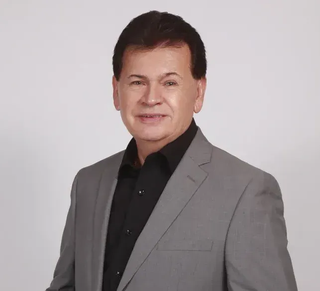 A man in a suit and black shirt smiles for the camera