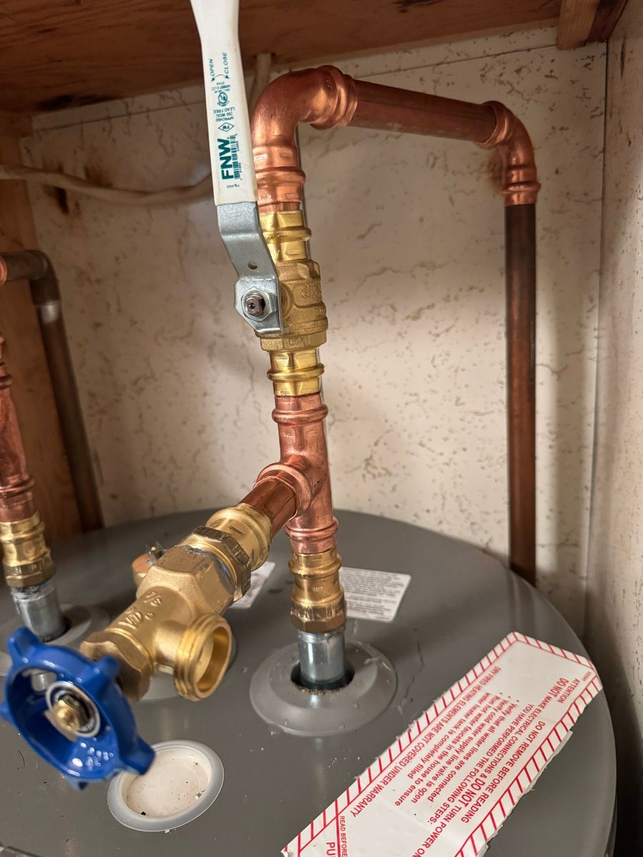 A close up of a water heater with copper pipes and a blue valve.
