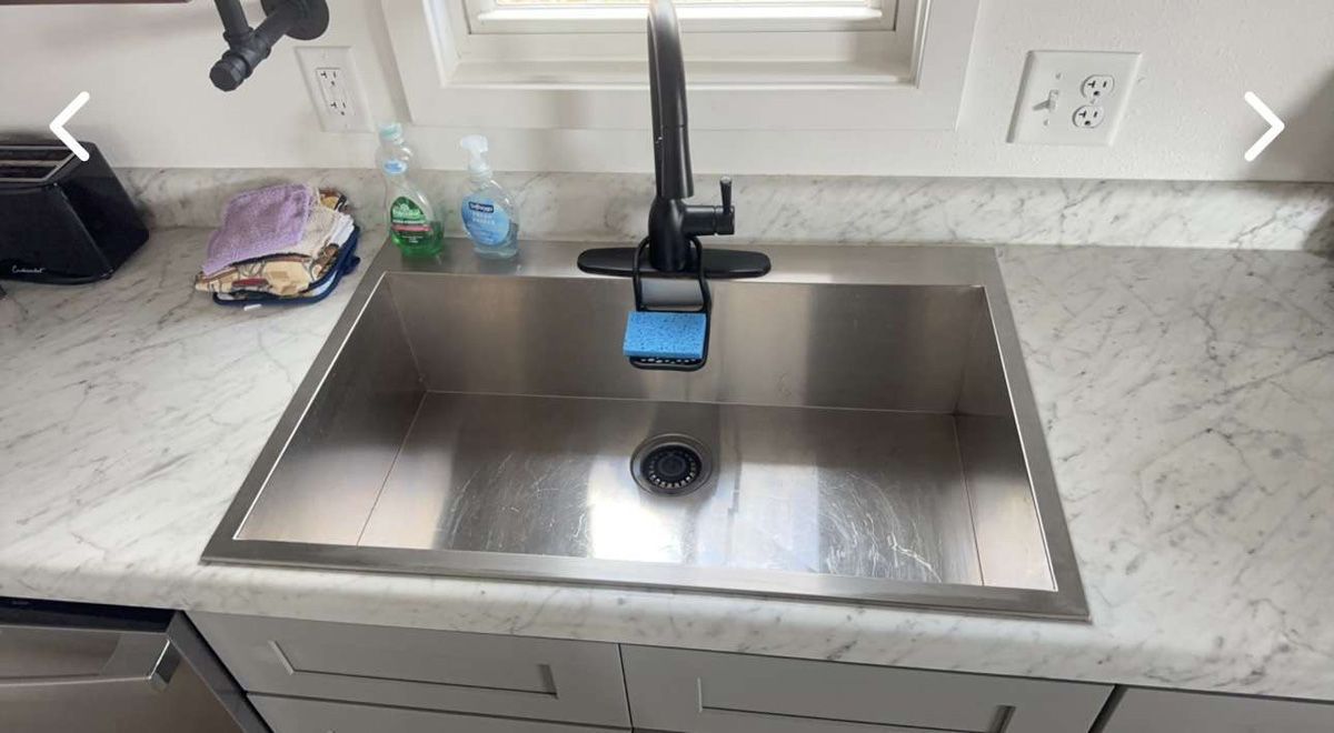 A stainless steel kitchen sink with a black faucet.