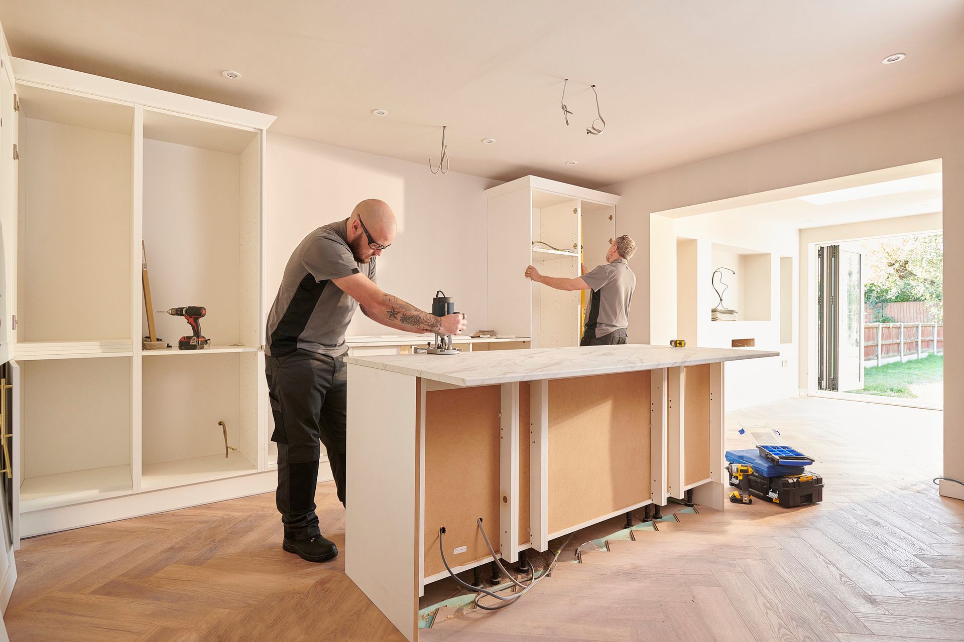 Two workers installing a kitchen island and cabinets in a room with wood flooring.