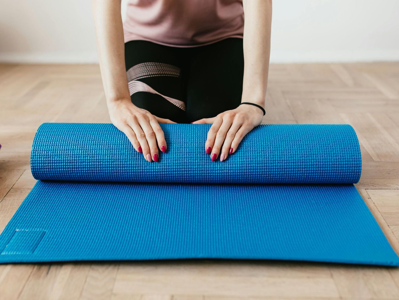 Woman rolling out a blue yoga mat on a wooden floor.