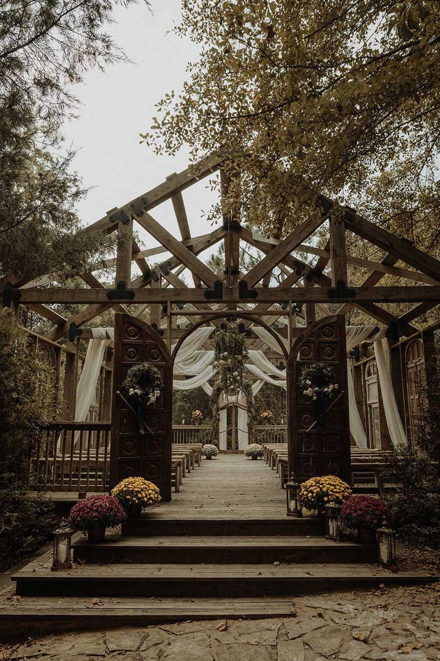 Outdoor wedding ceremony site with wooden structure, floral decorations, and draped fabric.