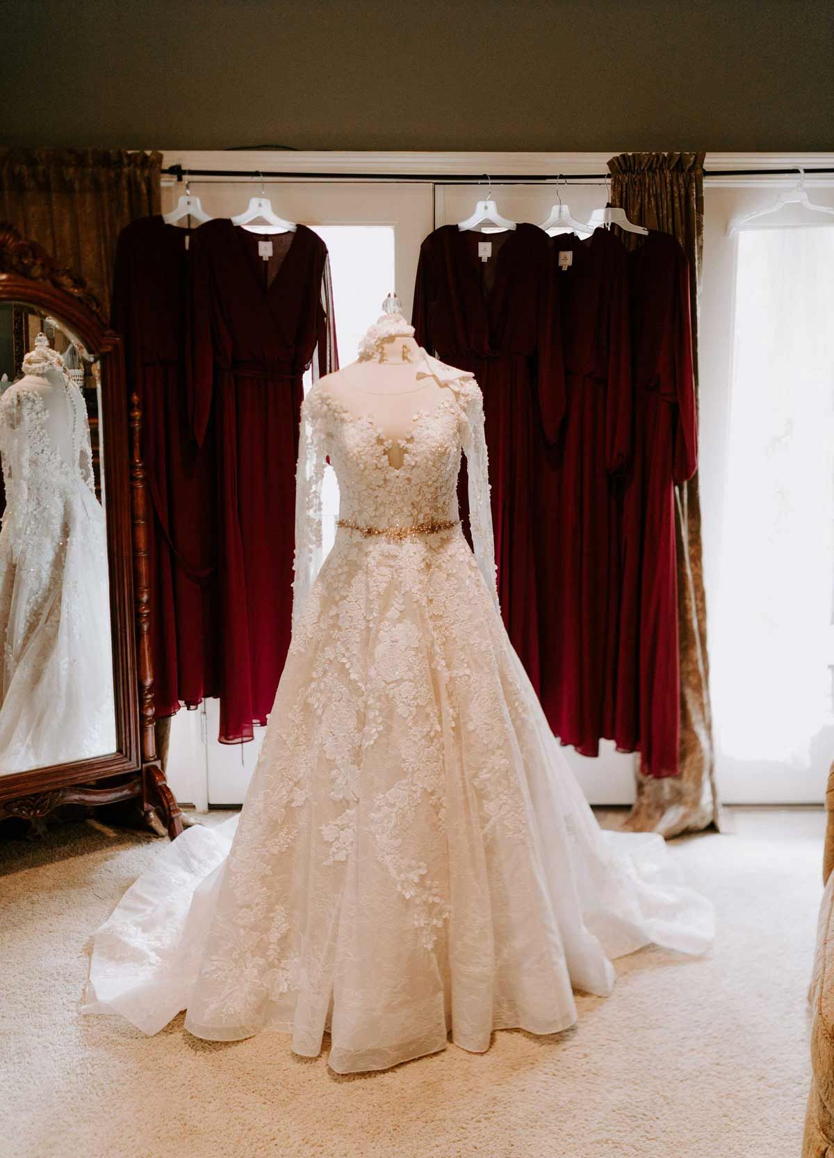 Wedding gown on a mannequin with burgundy bridesmaid dresses in the background.