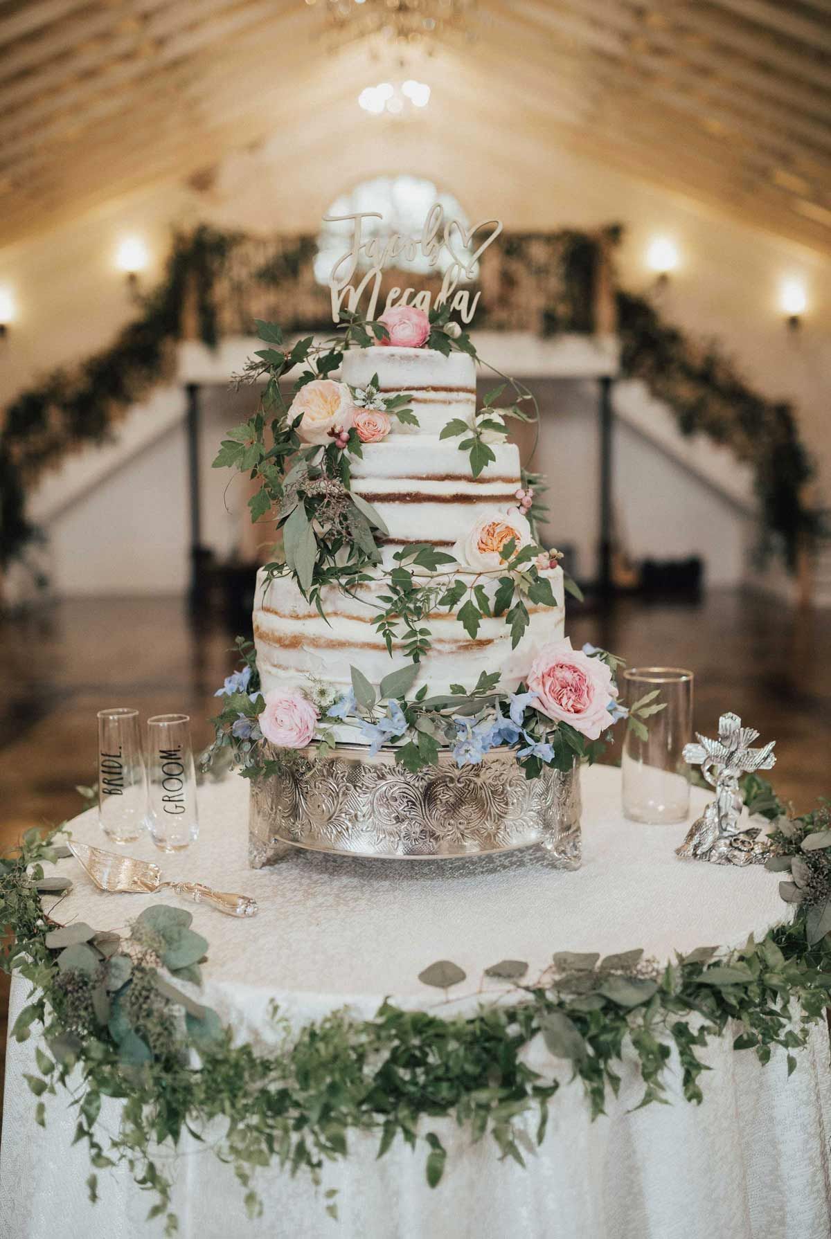 Five-tiered wedding cake with floral decorations on a sparkly table in a rustic venue.