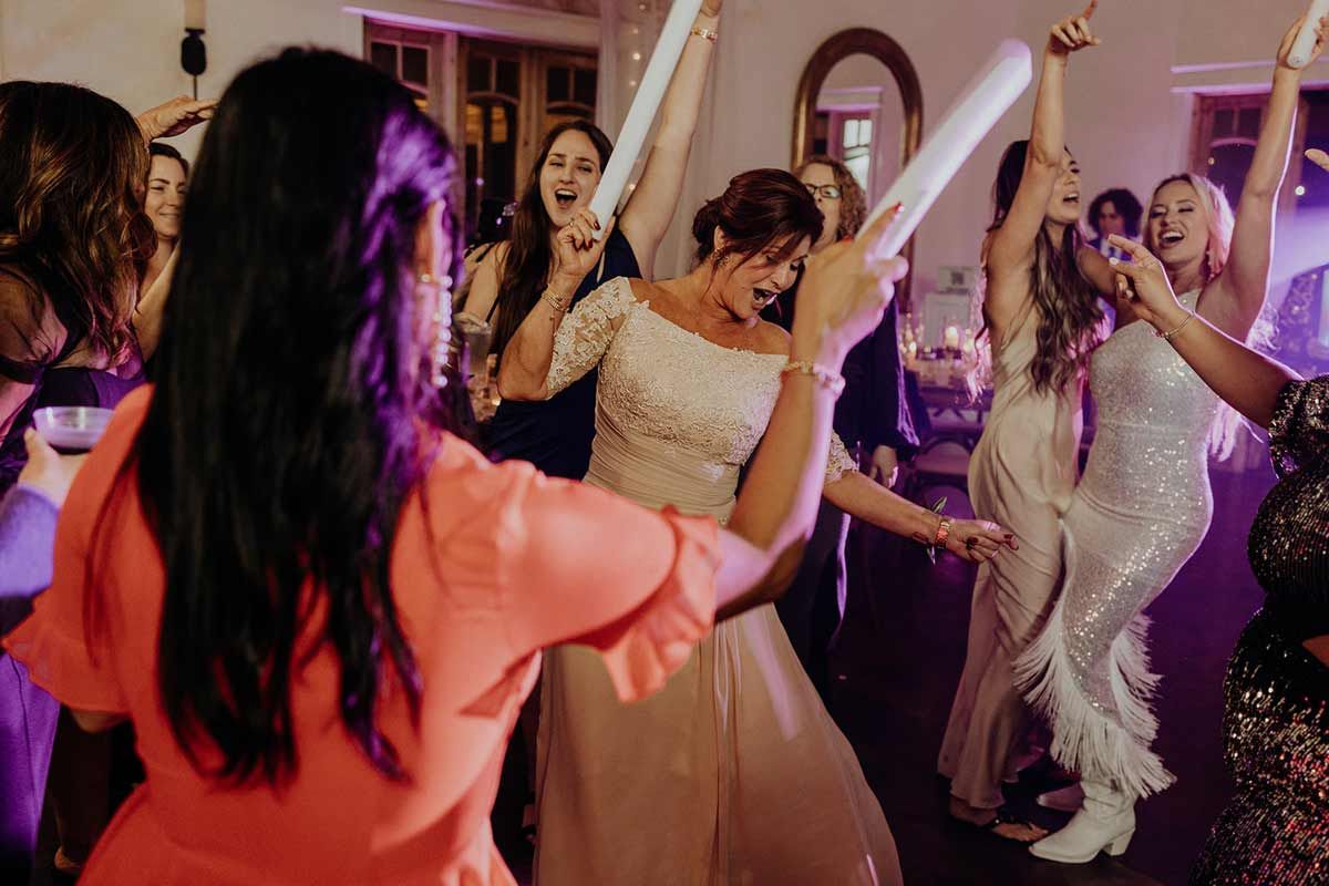 People dancing at a wedding reception; bride center in white dress, friends with light batons.