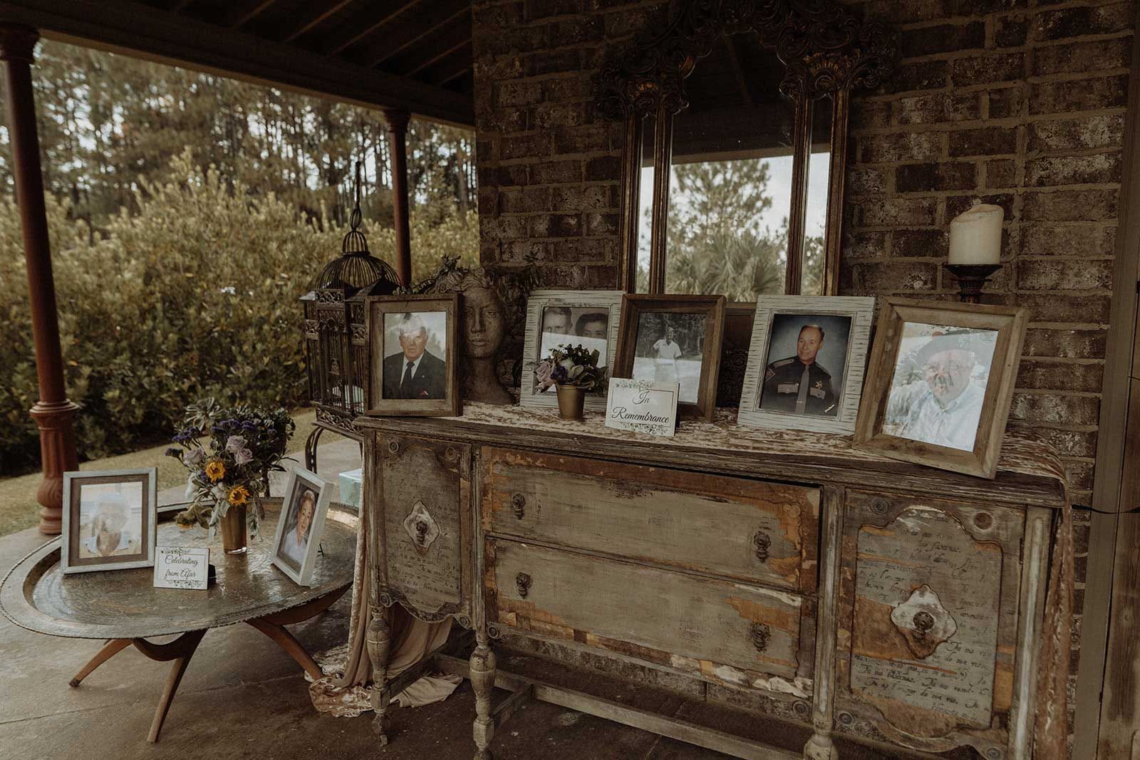 Antique dresser displays framed photos, under a brick covered porch.