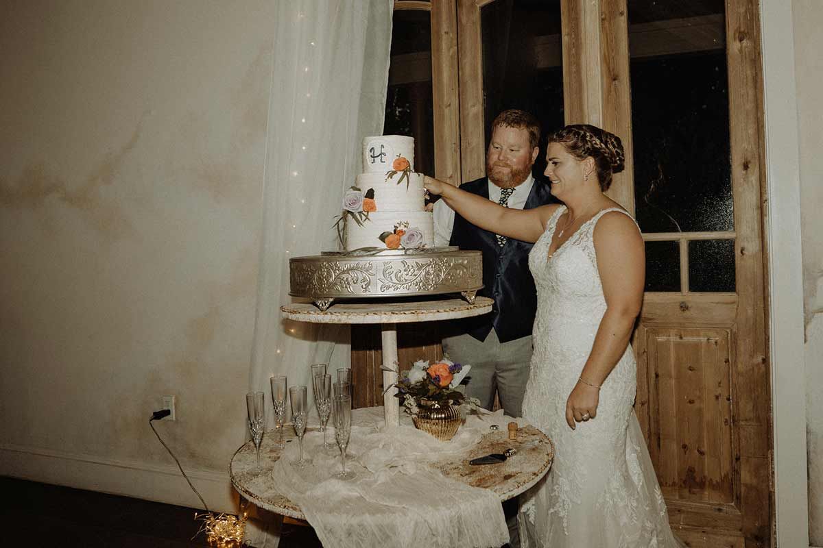 Bride and groom cutting wedding cake at reception, decorated with flowers and butterflies.