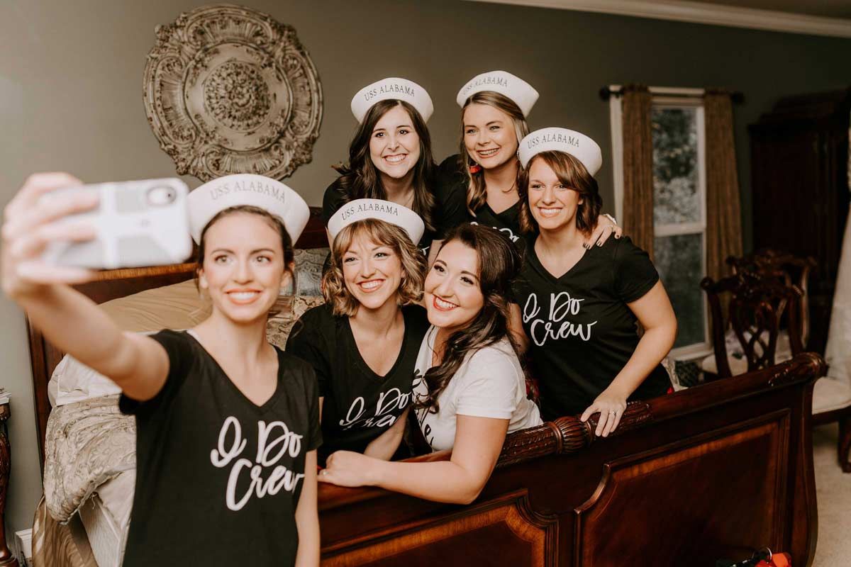 Group of women in matching shirts and hats taking a selfie in a bedroom.