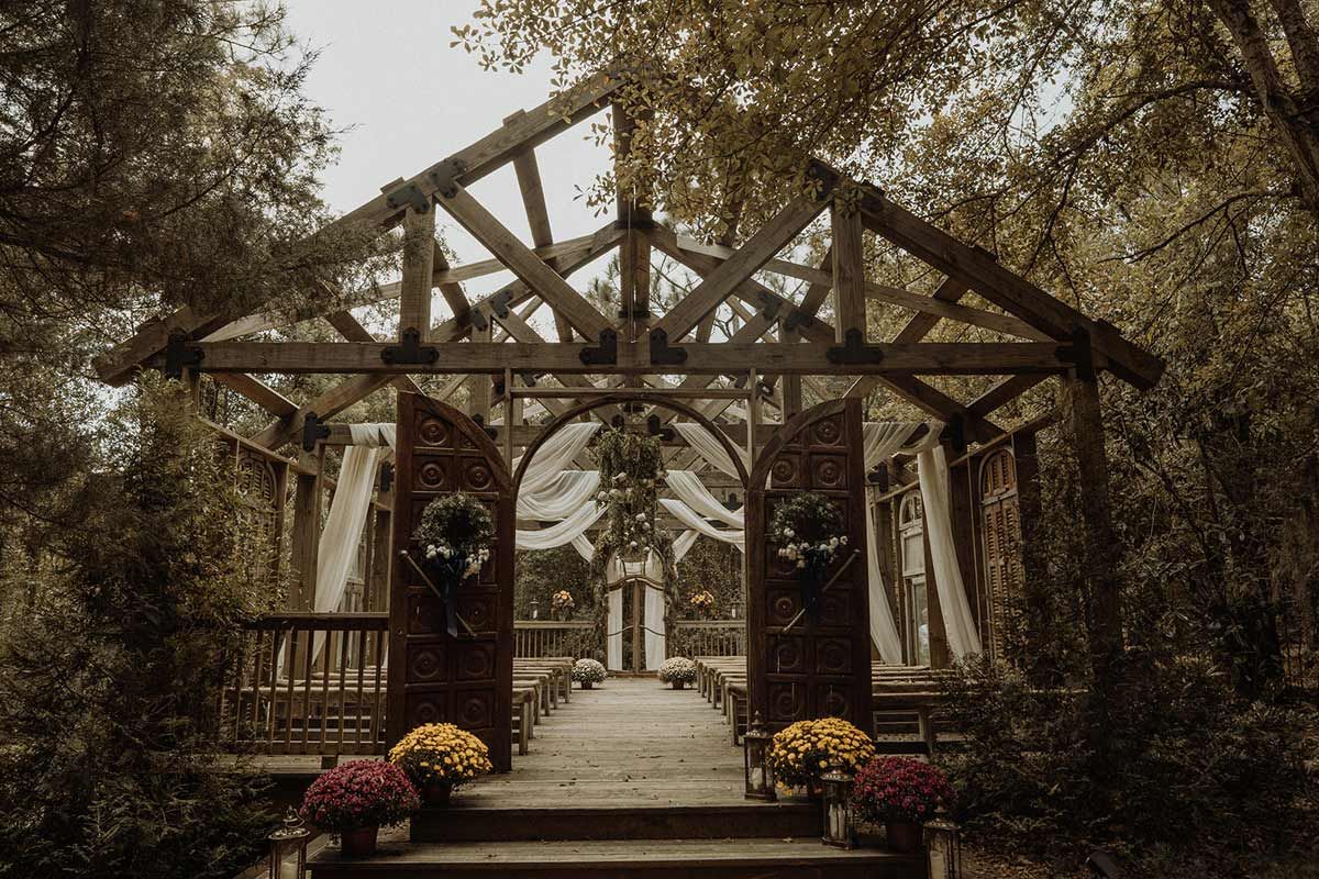 Wooden arbor in a forest setting decorated for a wedding ceremony; floral accents, white draping.