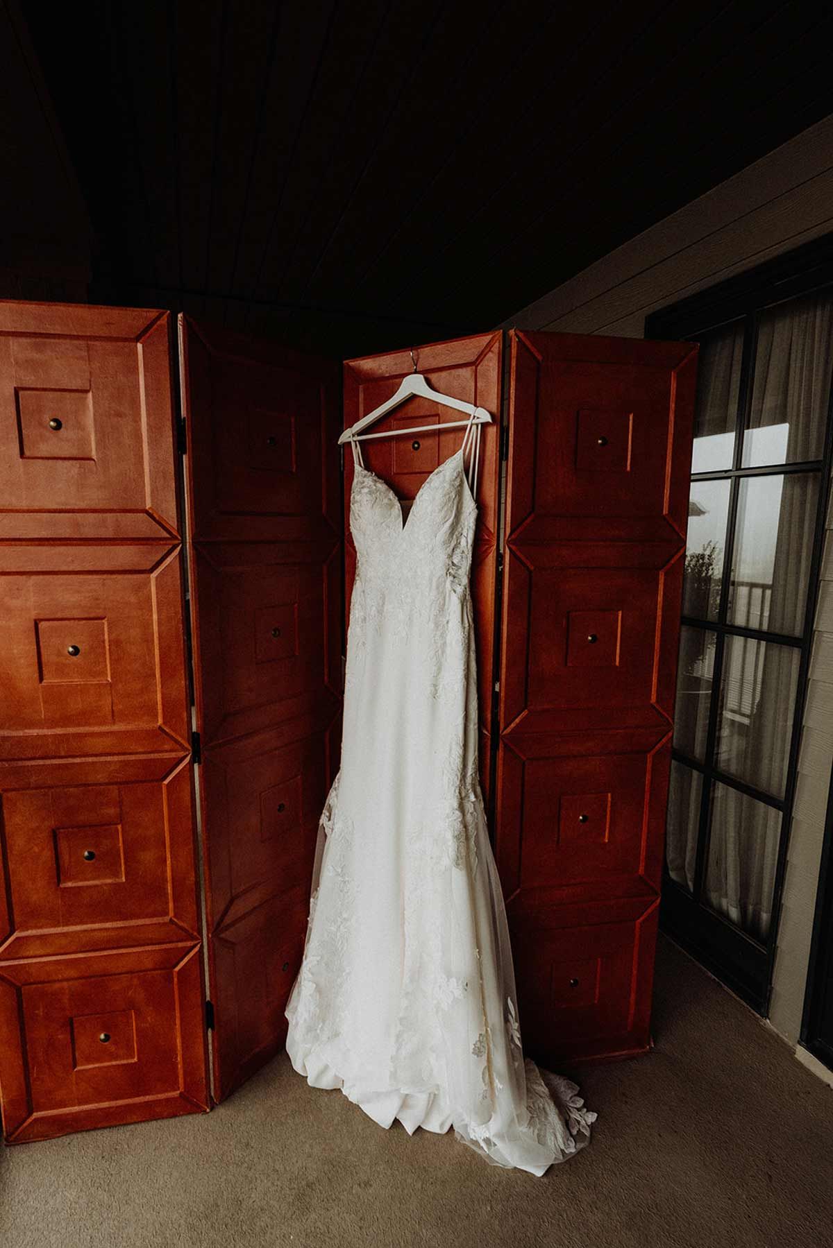Wedding dress hanging on a white hanger, against a red wooden screen, with a balcony view.