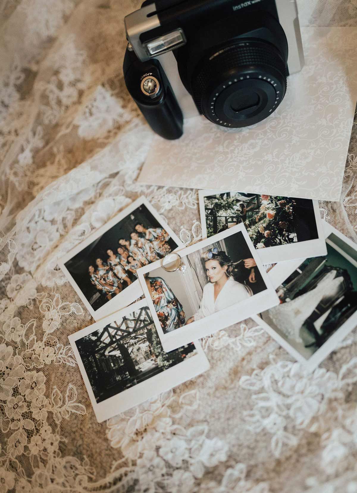 Black instant camera on white lace fabric with scattered polaroid photos.