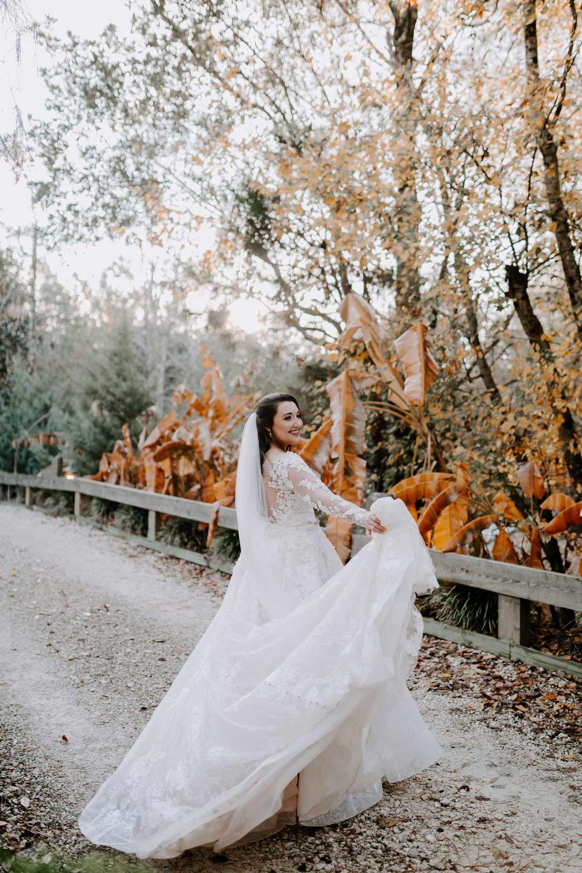 Bride in white gown twirling outdoors near pumpkins; autumn trees in background.