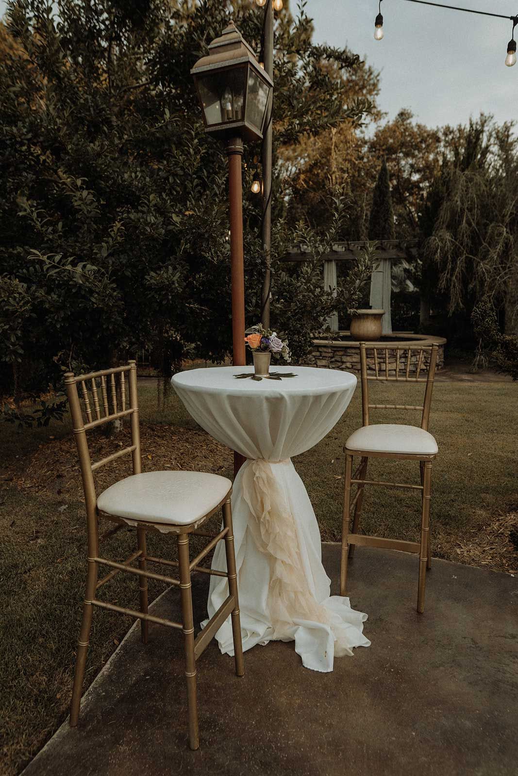 Outdoor cocktail table with draping, gold chairs, and a lamp post.