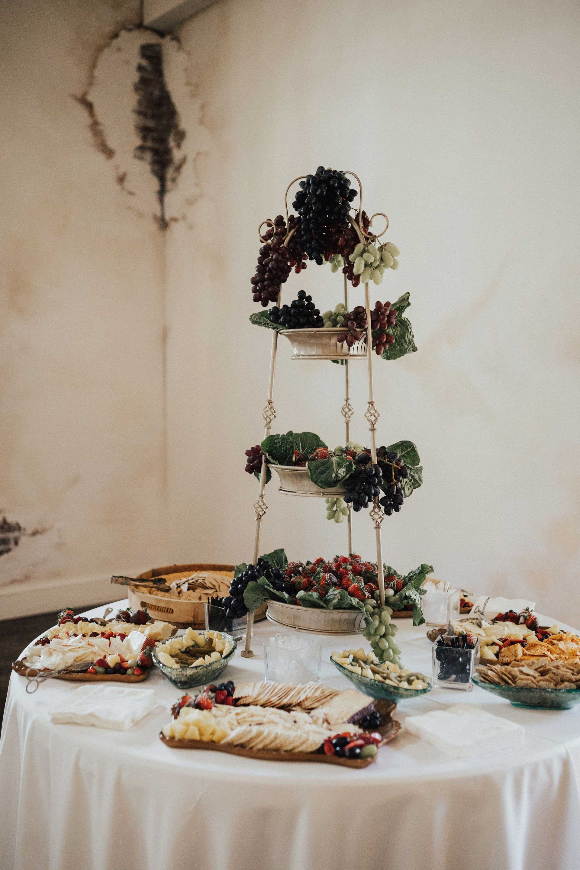 A table with food, including grapes on a tiered stand, in a room with peeling plaster.