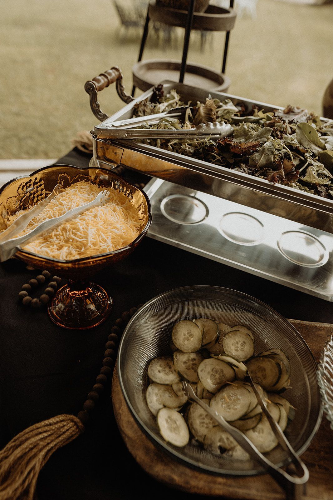 Buffet spread: Salad, cheese, and pickles on a dark table, with serving utensils.