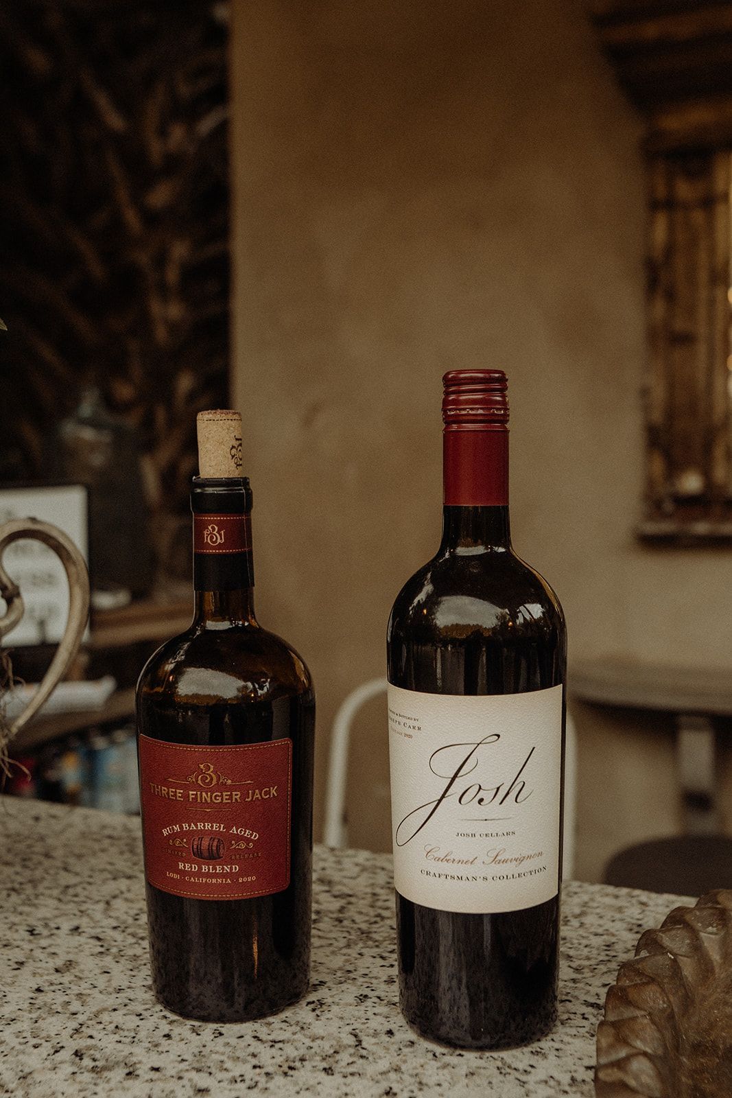 Two bottles of red wine on a counter: one with a cork, the other with a Josh label.