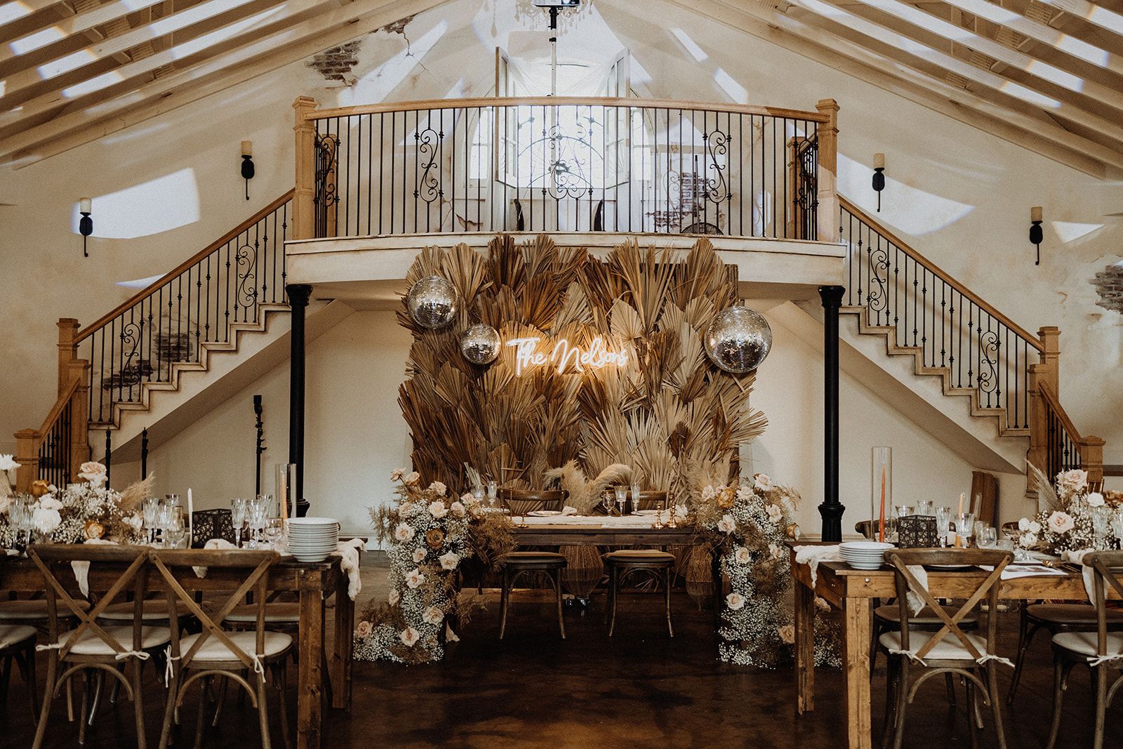 Wedding reception setup: wooden tables, chairs, and decor with a stage.