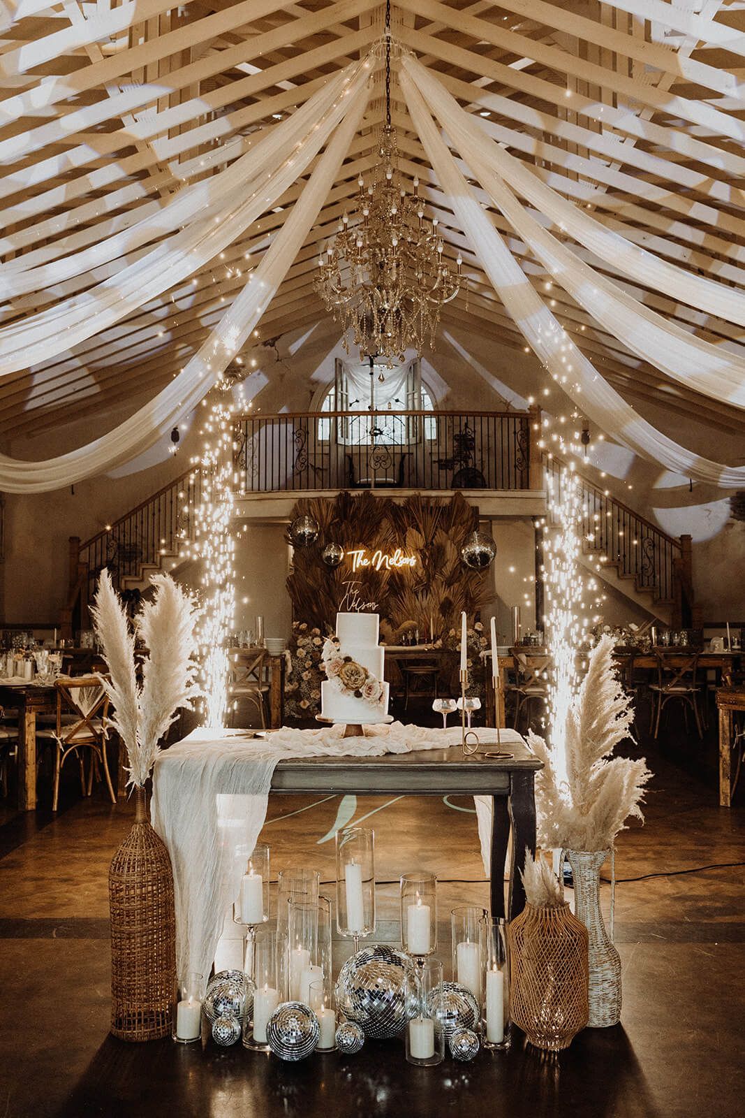 Wedding reception with a cake table, draped fabrics, and sparkling lights.