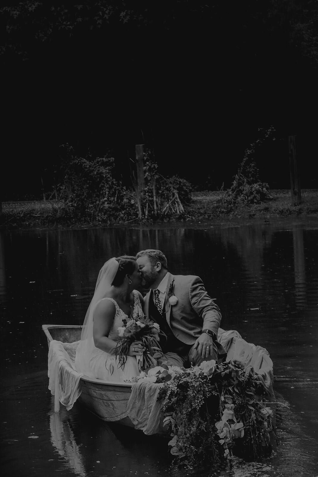 Couple kissing in a rowboat on a pond, wedding attire, flowers, dark background.