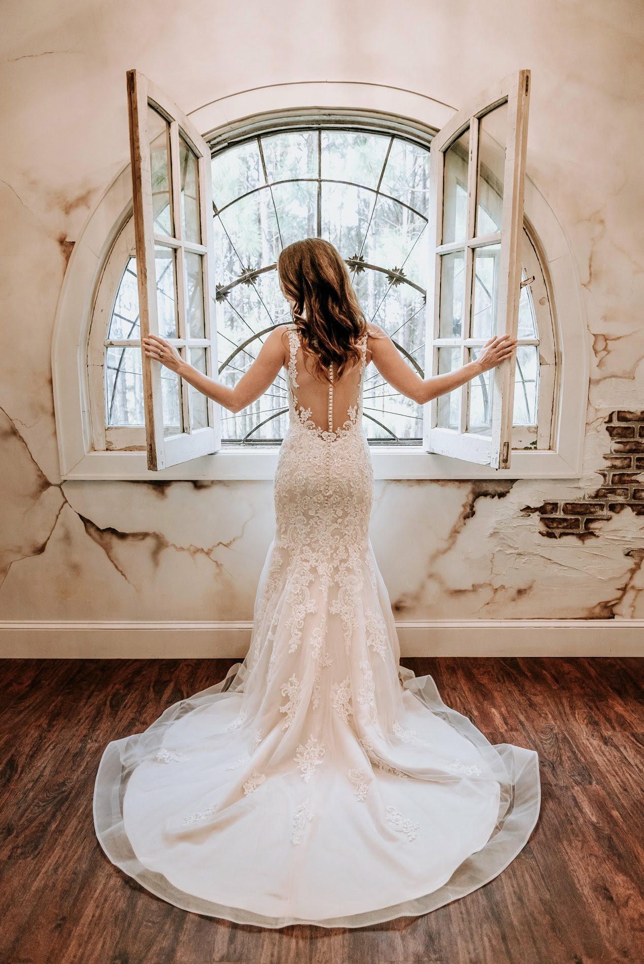 Woman in wedding dress opening window, arms outstretched, interior shot.
