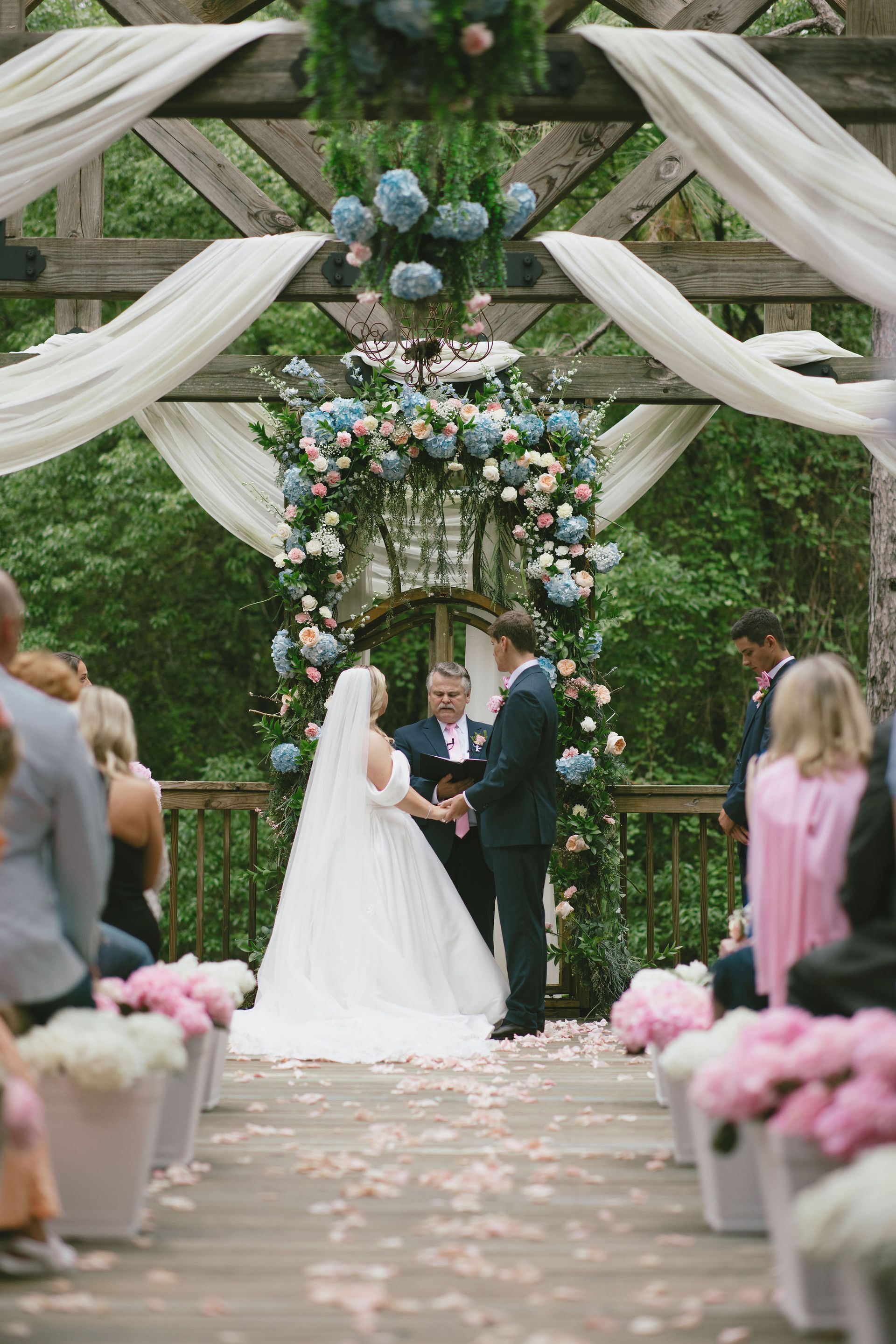 Wedding ceremony: couple exchanging vows under a floral archway, guests seated.