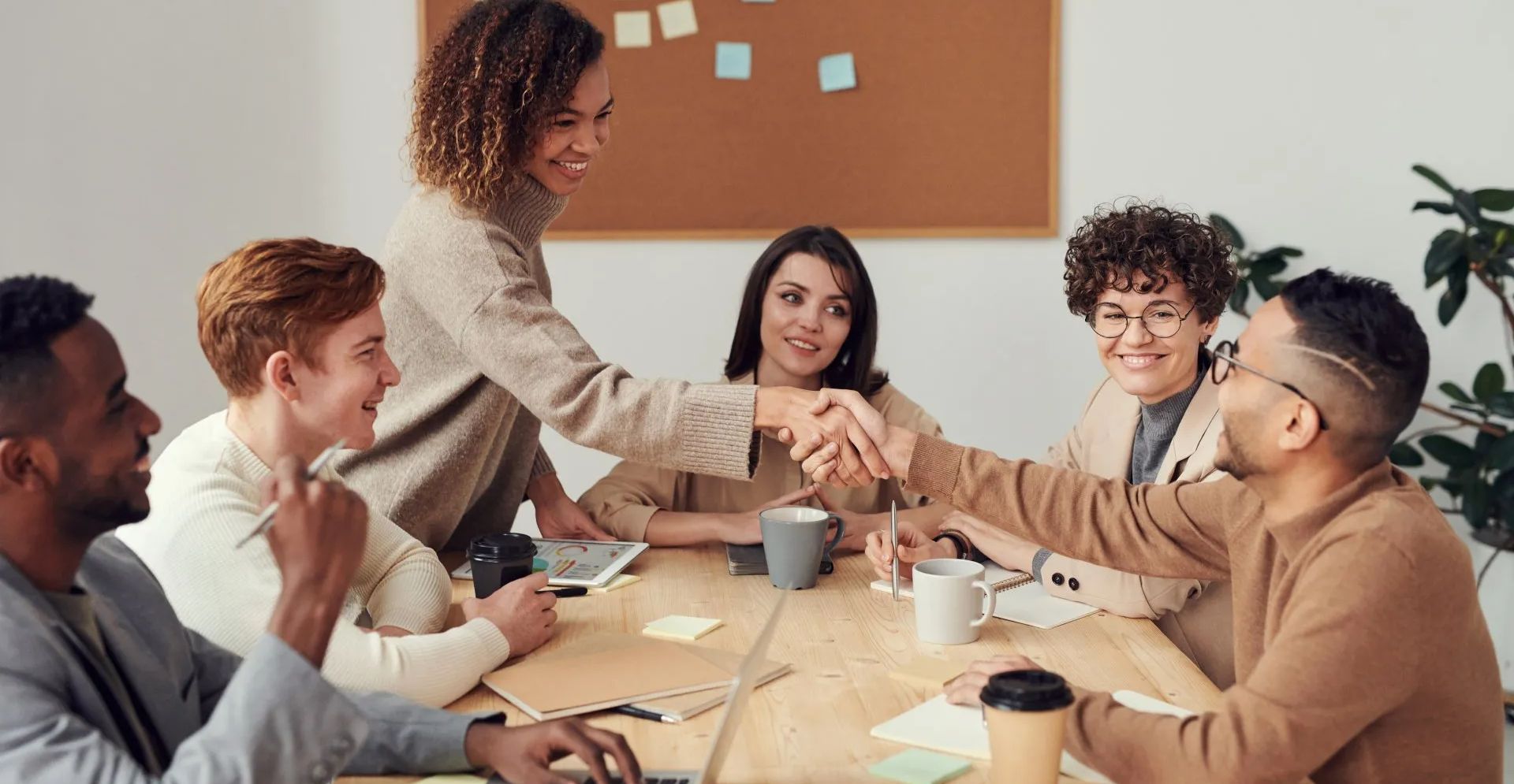 A group of people are sitting around a table shaking hands.