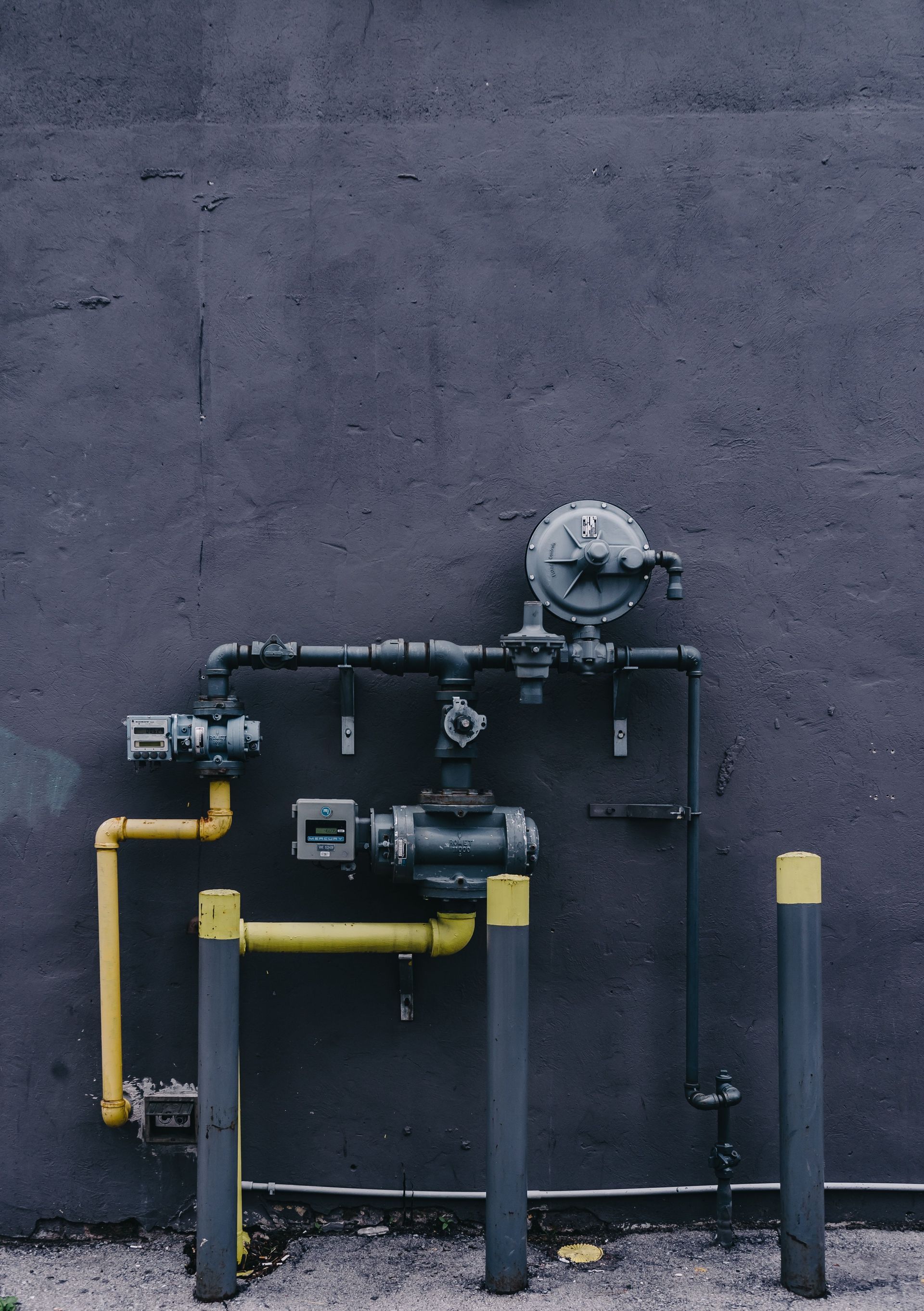 Yellow gas pipes and meter against a dark concrete wall
