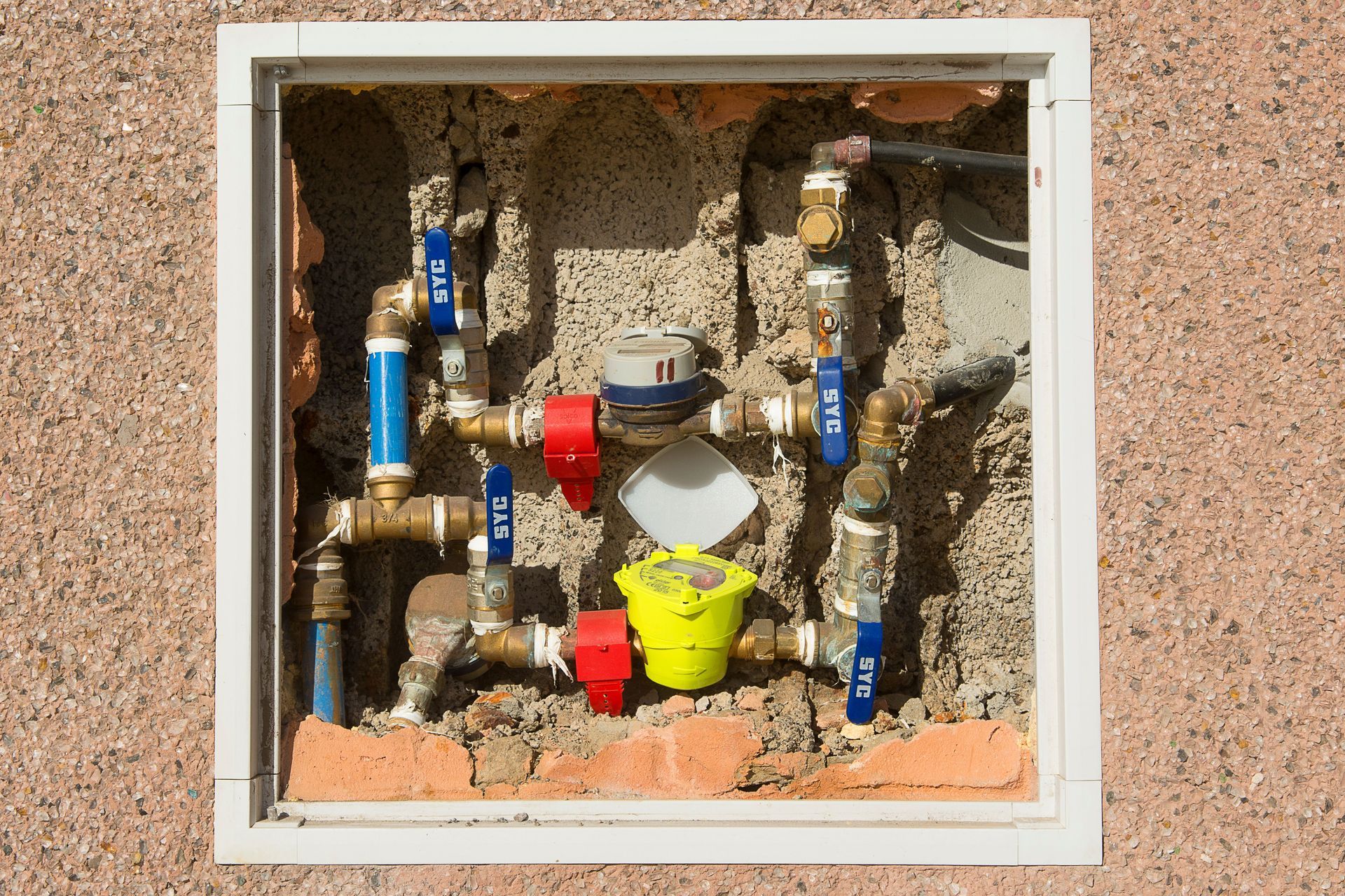 Water meter and pipes inside a wall access box, with red, blue, and brass valves.