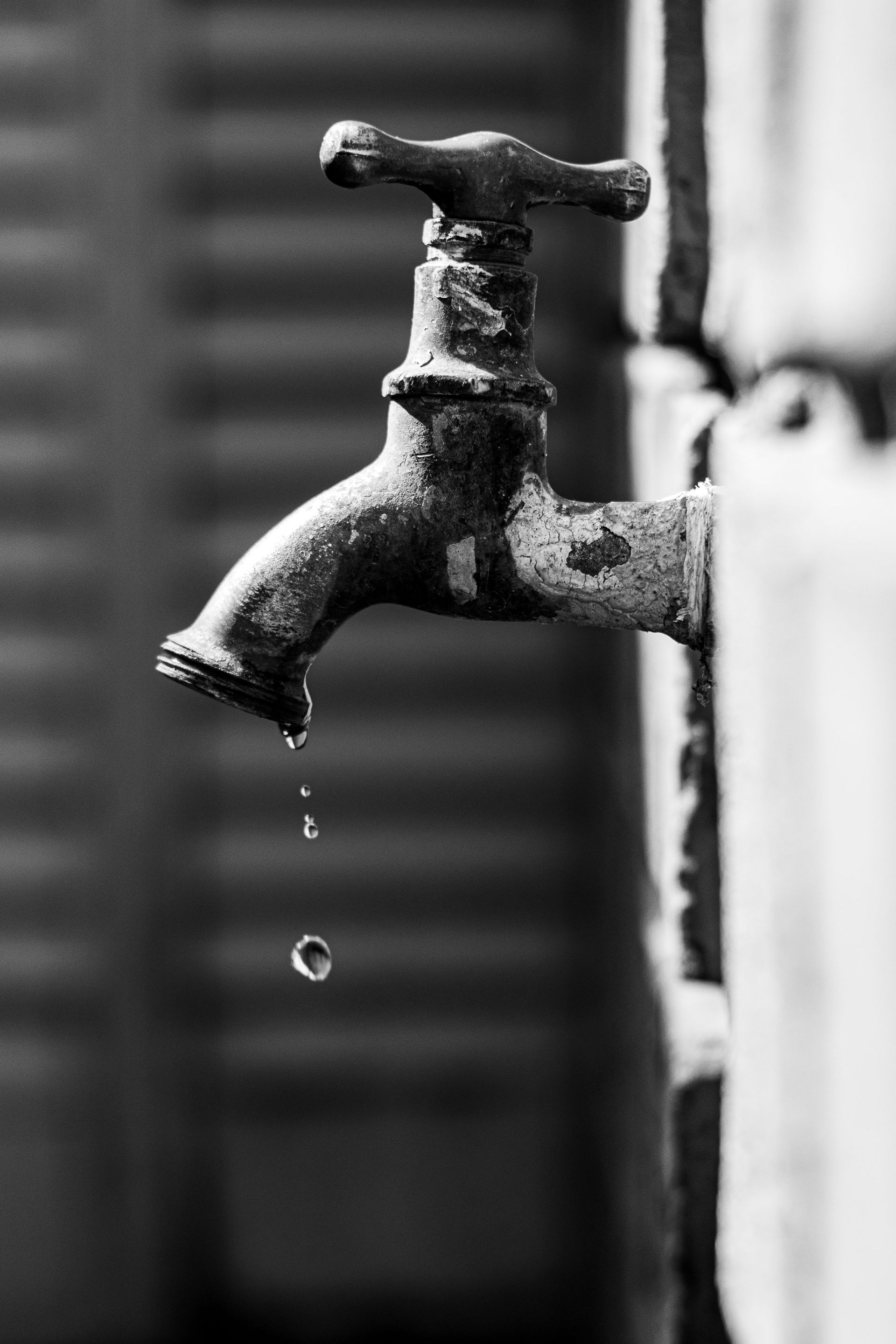 Black-and-white close-up of a dripping outdoor faucet against a blurred background