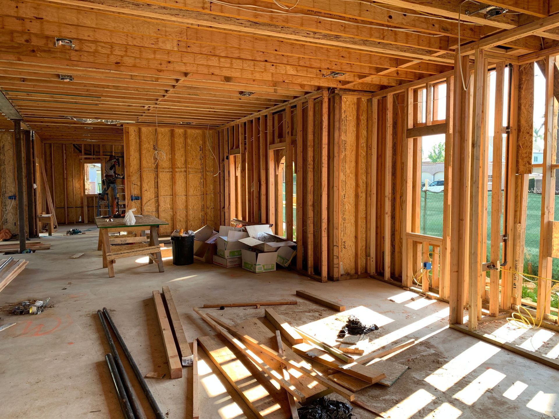 Interior of a house under construction with exposed wooden framing, sunlight, and строитель materials scattered on the floor