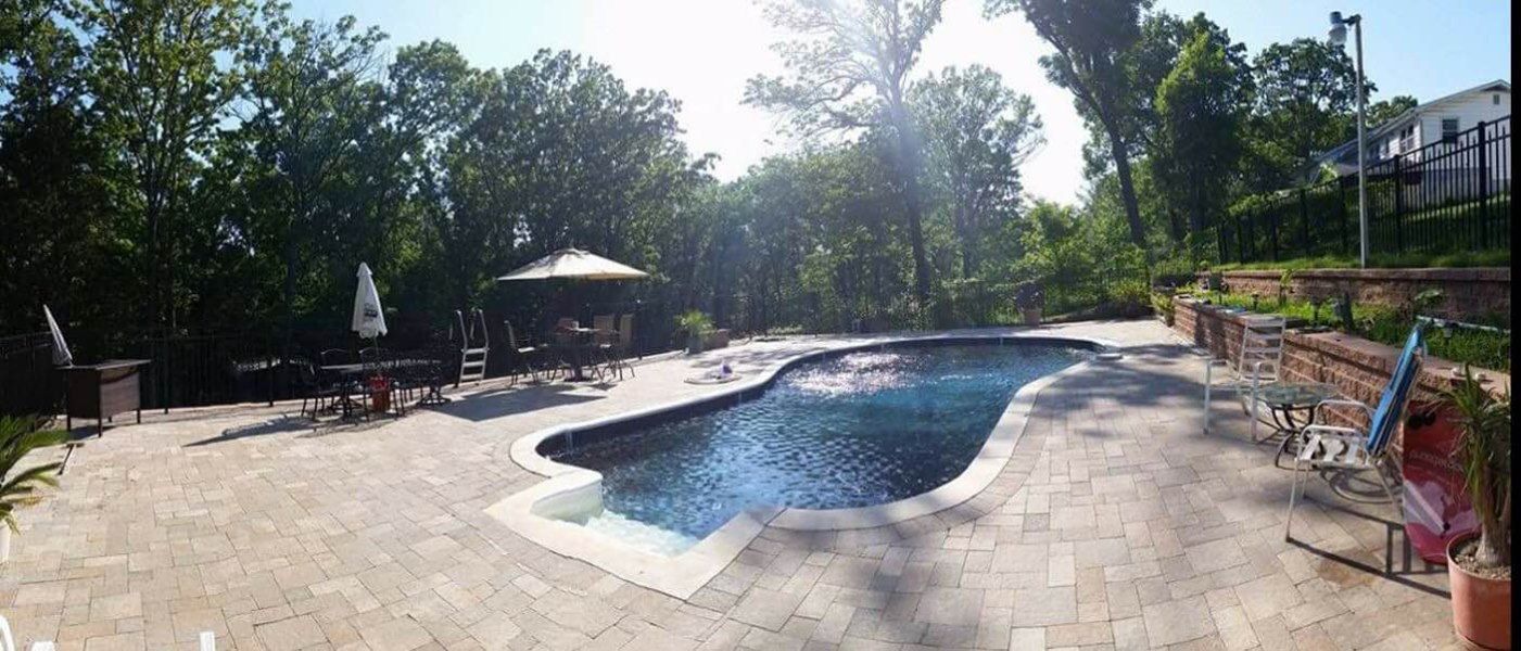 Backyard with a pool, patio, trees, and outdoor furniture on a sunny day.