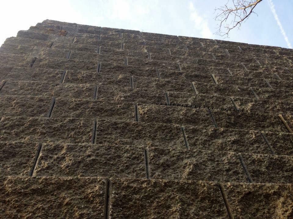A tall, textured brown retaining wall made of rectangular blocks against a blue sky.