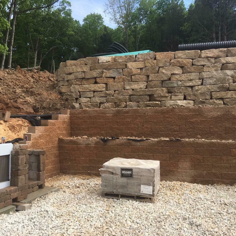 Retaining walls under construction with stone and concrete blocks, gravel ground, and a pallet of blocks.