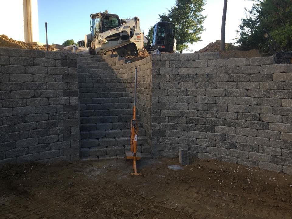 A retaining wall with stairs, and a bobcat working, outdoors.