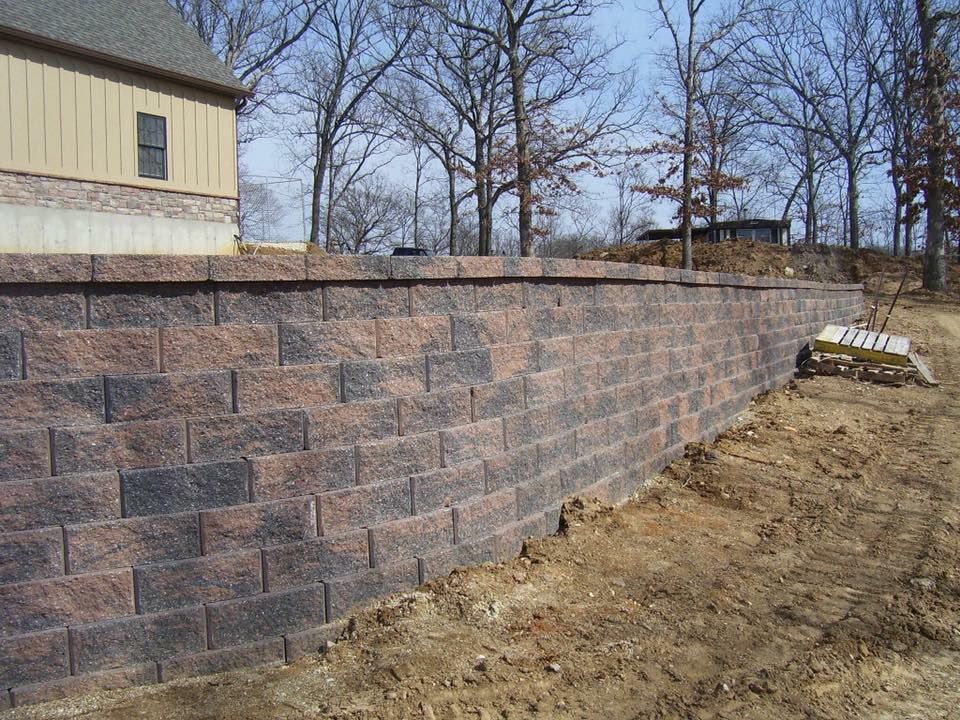Brick retaining wall beside a tan house, built into a hillside.