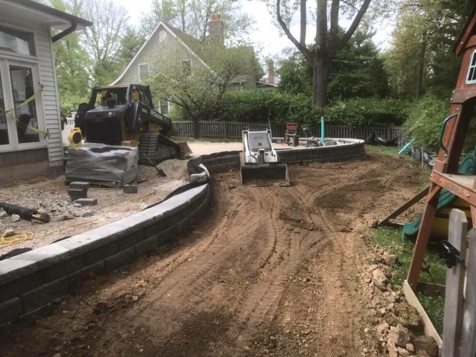 Construction site: a bulldozer and skid steer grading dirt in a backyard with a retaining wall.