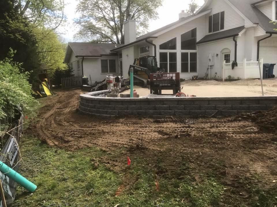 Backyard under construction with retaining wall, dirt, machinery, and a house.